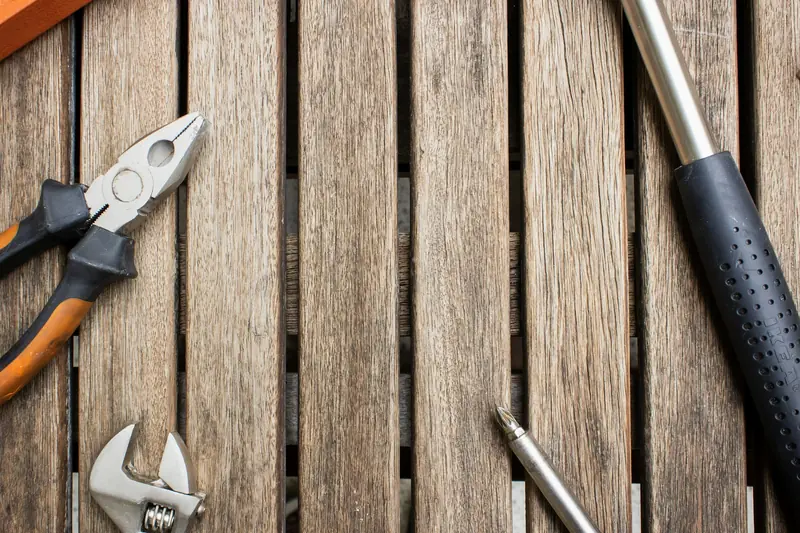 Pliers, an adjustable wrench, and screwdrivers on a wooden workbench