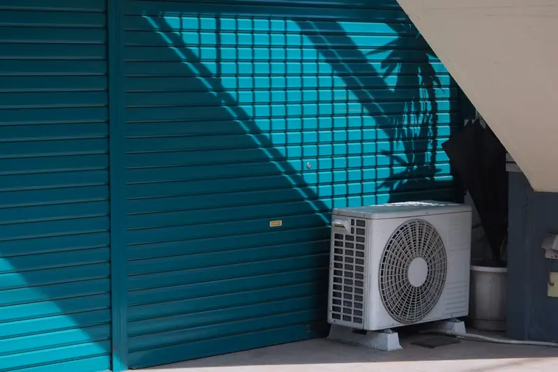Outdoor air conditioning unit beside a teal roll-up door